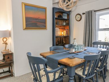 A dining area with a wooden table and blue chairs with cushions next to a window with grey curtains in Marsh Villa in Silloth
