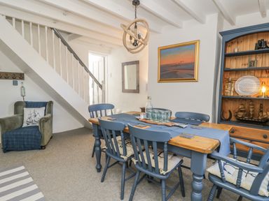 A dining room with a wooden table and blue chairs under a staircase at Marsh Villa in Silloth