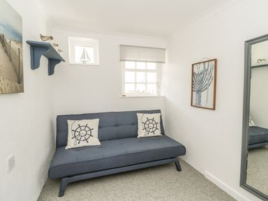 A small room with a blue sofa and nautical cushions a window with a sailboat decoration a framed lobster print a mirror and a blue wall shelf at Marsh Villa in Silloth