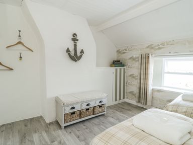 A bedroom with two beds a cushioned storage bench wall hooks with hangers and a window at Marsh Villa in Silloth
