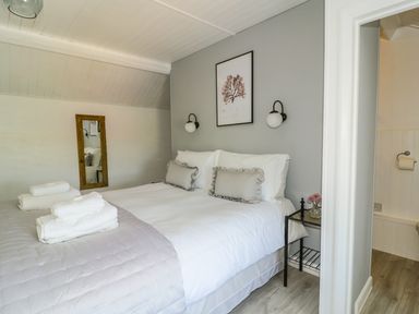 A bedroom with a bed made with white linens and gray pillows a wooden framed mirror on the wall and a small black bedside table with flowers at Marsh Villa in Silloth