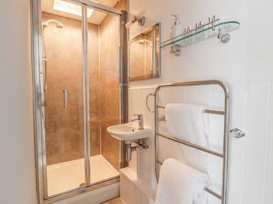 A bathroom with a glass shower enclosure sink mirror towel rack and shelves with toiletries at Marsh Villa in Silloth