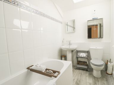 A bathroom with a bathtub sink toilet mirror and small shelf with towels at Marsh Villa in Silloth