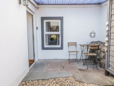 A small outdoor patio with two wooden chairs and a table next to a window at Marsh Villa in Silloth