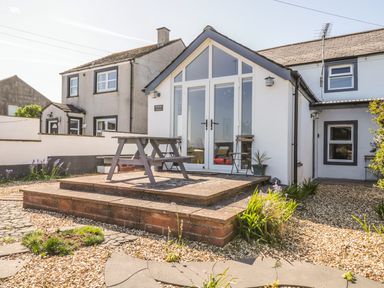 A white house with large glass doors and a wooden picnic table on a raised brick patio at Marsh Villa in Silloth