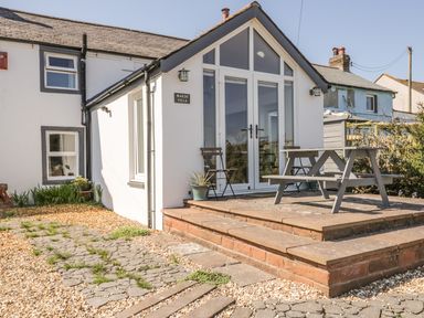 The exterior of a white building with a patio area featuring a picnic table and chairs at Marsh Villa in Silloth