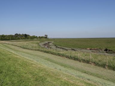 A grassy field with a small creek running through it and a fence alongside at Marsh Villa in Silloth