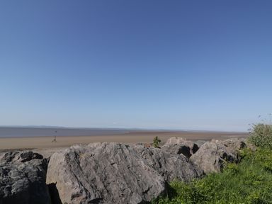 A beach with large rocks and grass in the foreground and the sea and blue sky in the background at Marsh Villa in Silloth