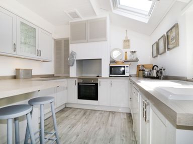 A kitchen with gray stools an oven microwave kettle and sink at Marsh Villa in Silloth