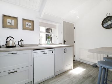 A kitchen with white cabinets a dishwasher a kettle and framed animal pictures on the wall at Marsh Villa in Silloth