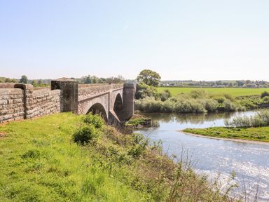 A stone bridge over a river with grass and trees around in a rural area at Victoria Cottage in Norham