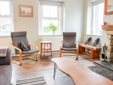 A sitting area with two armchairs a wooden coffee table a side table a bench with cushions and a stone fireplace at Victoria Cottage in Norham