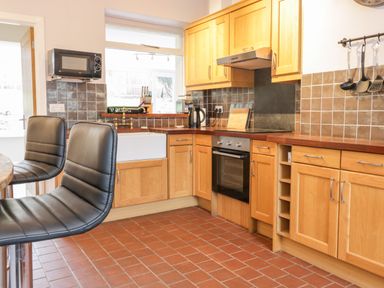 A kitchen with wooden cabinets a built-in oven black bar stools and cooking utensils at Victoria Cottage in Norham