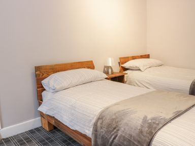A bedroom with two single beds with wooden headboards and a small wooden nightstand with a lamp between them at Victoria Cottage in Norham