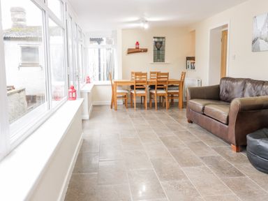 A dining area with a wooden table and six chairs and a brown leather sofa at Victoria Cottage in Norham