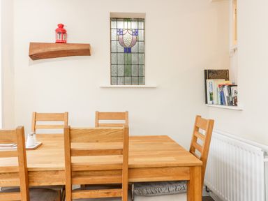 A dining area with a wooden table and chairs stained glass window and books on a ledge at Victoria Cottage in Norham