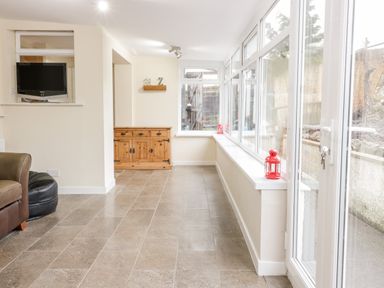A hallway with tiled floor windows on one side and a wooden cabinet on the far wall at Victoria Cottage in Norham