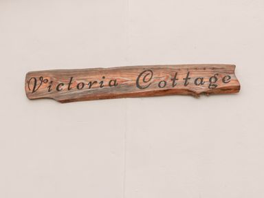 A wooden sign with Victoria Cottage written on it mounted on a white wall at Victoria Cottage in Norham