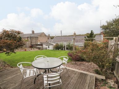 A garden with a circular glass table and four metal chairs on a wooden deck at Victoria Cottage in Norham
