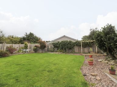A garden with a green lawn potted plants a wooden fence and outdoor seating at Victoria Cottage in Norham