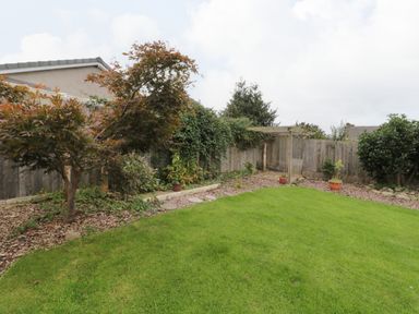 A backyard garden with green lawn trees potted plants and a wooden fence at Victoria Cottage in Norham