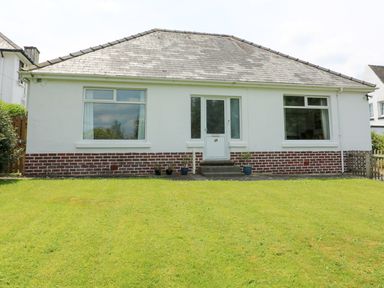 A white bungalow with two large windows and a central door with steps leading to a lawn at White Thorns in Haverfordwest