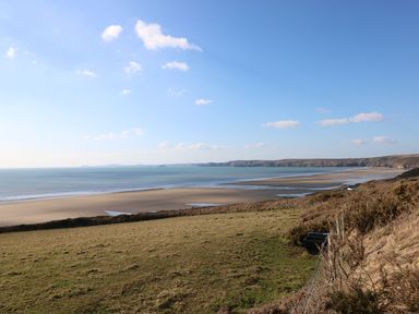 A coastal landscape with sandy beach water and hills with grassland at White Thorns in Haverfordwest