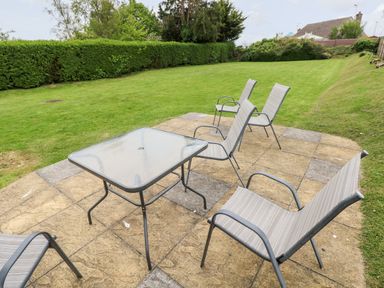An outdoor patio with a glass table and four metal chairs overlooking a lawn at White Thorns in Haverfordwest