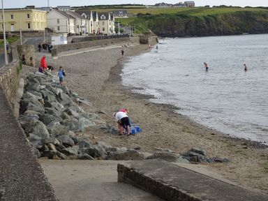 A beach with people on the sand and in the water near houses and cliffs at White Thorns in Haverfordwest