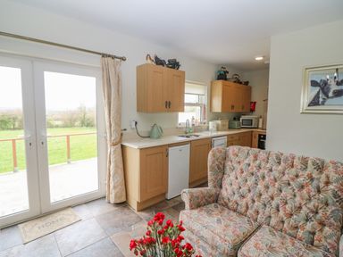 A kitchen and sitting area with floral upholstered sofa red flowers kitchen cabinets and glass doors leading outside at Shandrum Brook in Charleville