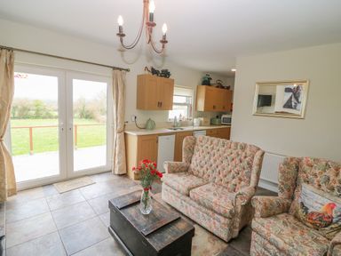 A living room with floral sofas and a wooden chest as a coffee table next to a kitchen area with cabinets and appliances at Shandrum Brook in Charleville