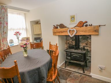 A dining room with a table covered with a tablecloth and flowers a wood stove and a window with floral curtains at Shandrum Brook in Charleville