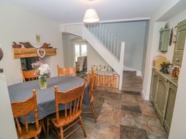 A dining room with wooden chairs around a table with a vase of flowers a staircase with a built in bench and a cabinet with decorative items at Shandrum Brook in Charleville