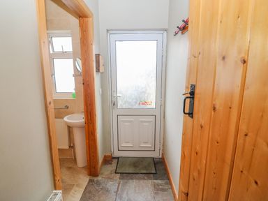 A hallway with a white back door and a wooden coat rack on the right wall adjacent to a wooden door and a small bathroom with a window and a pedestal sink at Shandrum Brook Charleville
