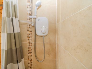A shower area with a showerhead electric water heater and beige tiled walls at Shandrum Brook in Charleville