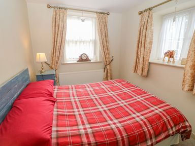 A bedroom with a bed covered in a red plaid blanket next to two windows with floral curtains at Shandrum Brook in Charleville