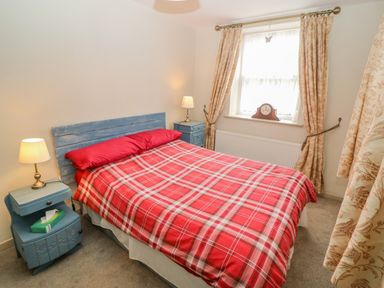 A bedroom with a bed covered with a red plaid blanket and two blue nightstands with lamps at Shandrum Brook in Charleville