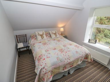 A bedroom with a bed covered in floral quilt and deer pillows beside a window with a clock on the sill at Shandrum Brook in Charleville