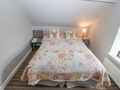 A bedroom with a bed covered with a floral quilt two pillows with deer design a wooden chair and a lamp on a bedside table at Shandrum Brook in Charleville