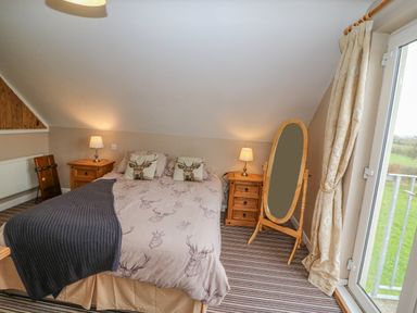 A bedroom with a double bed featuring deer-themed bedding and pillows two wooden bedside tables with lamps a wooden standing mirror and a glass door with curtains at Shandrum Brook in Charleville
