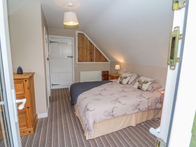 A bedroom with a double bed two wooden nightstands a wooden chest of drawers a lamp and a striped carpet at Shandrum Brook in Charleville
