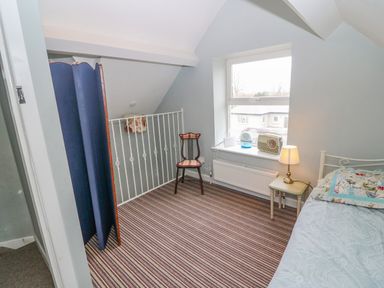 A small bedroom with a striped carpet a bed a bedside table with a lamp a chair a window with items on the sill and a blue room divider at Shandrum Brook in Charleville