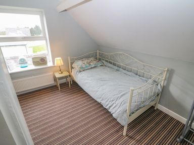 A bedroom with a metal frame bed a bedside table with a lamp a window with objects on the sill and striped carpet at Shandrum Brook in Charleville