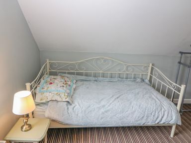 A bedroom with a single bed with a metal frame and a small table with a lamp at Shandrum Brook in Charleville