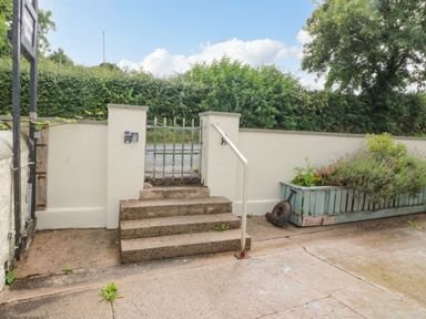 A concrete staircase with a metal handrail leading to a metal gate set in a white wall with a planter box on the right at Shandrum Brook in Charleville