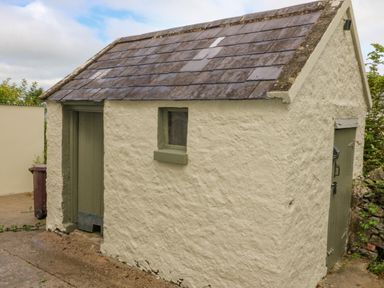 A small outbuilding with a textured white exterior green doors and a slate roof at Shandrum Brook in Charleville