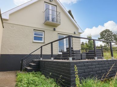 An outdoor patio area with black wicker furniture and railing attached to a beige house at Shandrum Brook in Charleville