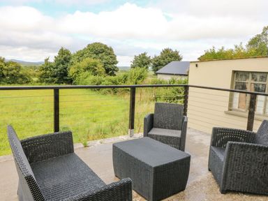 An outdoor patio with black wicker furniture including chairs and a table overlooking a grassy field at Shandrum Brook in Charleville