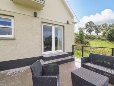 An outdoor patio with black wicker furniture and glass doors leading inside at Shandrum Brook in Charleville