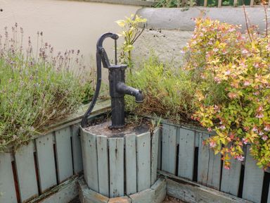 An outdoor corner wooden planter with an old hand water pump surrounded by plants and flowers at Shandrum Brook in Charleville